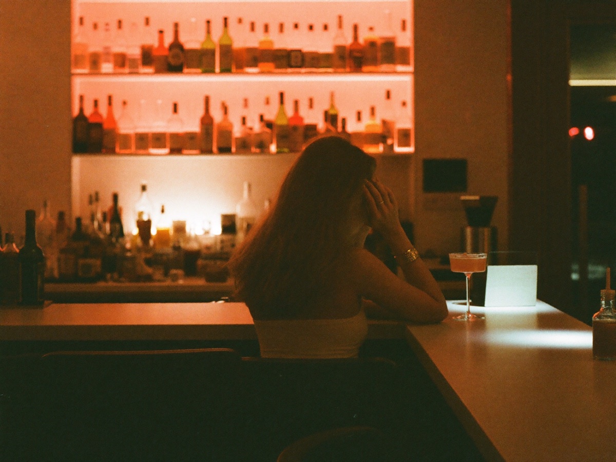 A woman alone at a rose-lit bar, late at night